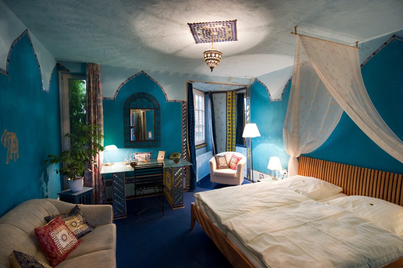 Themenzimmer: Indisches Gold Farbige Hotelzimmer mit blauem Anstrich, Bett, Sessel und Schreibtisch.