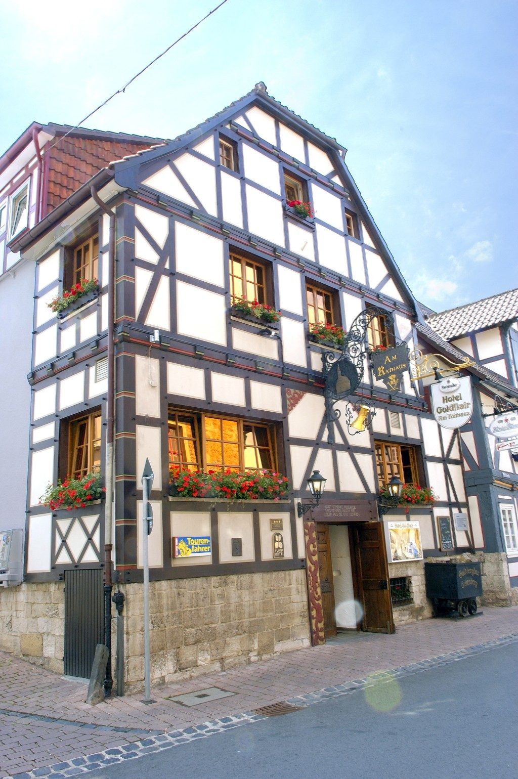 Frontansicht Hotel Goldflair Fachwerkhaus mit weißen Wänden, dunklem Holz und blühenden Fensterkästen. Frontansicht Hotel Goldflair